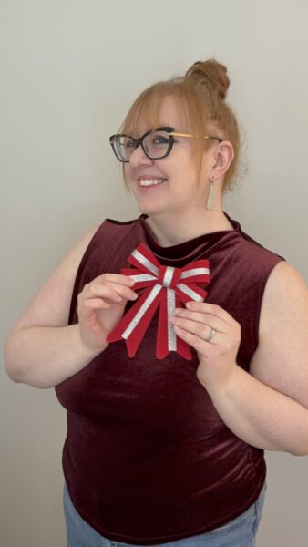 Stacey holding a red and silver bow and smiling